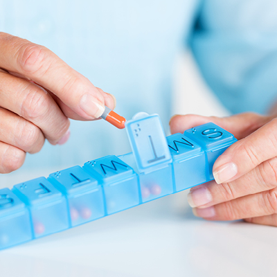 person putting pills into daily container 